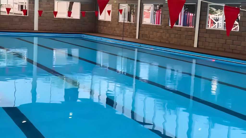 Indoor Swimming Pool with Blue Water, Black Lane Lines, and Red Pennant Banners Hanging Above. - Adelante Mty