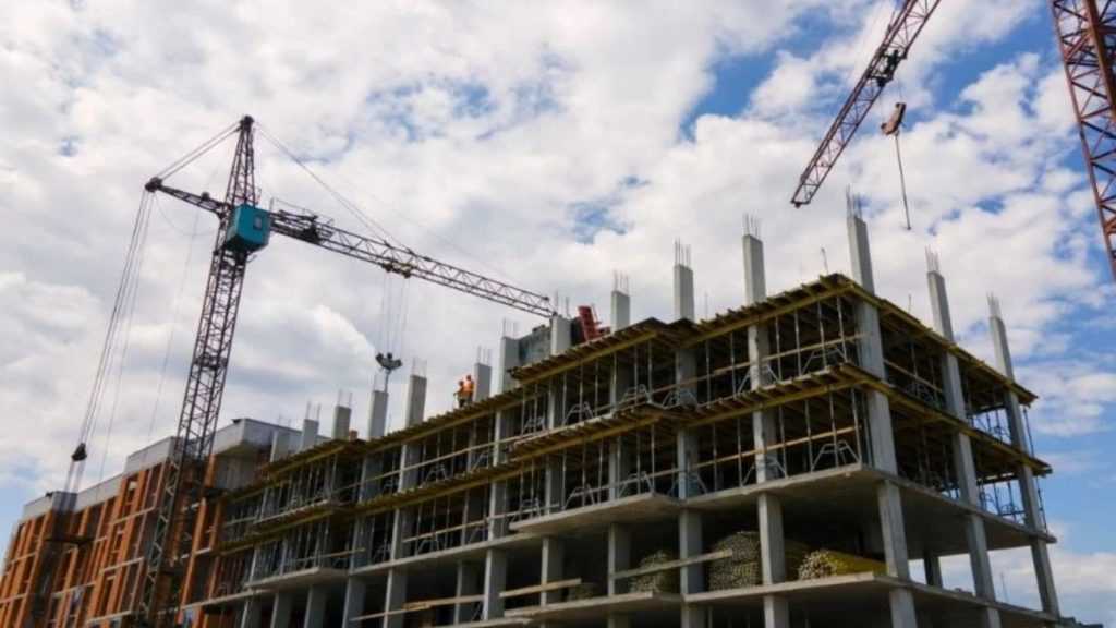 Construction Site with a Multi-story Concrete Frame and Cranes Overhead Under a Cloudy Sky. - Adelante Mty