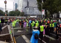 Crowd of People Wearing Bright Safety Vests Gather on a Closed City Street with Tall Modern Buildings in the Background. - Adelante Mty