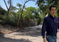Man in a Navy Shirt and Jeans Walks Along a Sunny, Tree-lined Walkway with a Wire Fence on the Left, Suggesting a Construction Area. - Adelante Mty
