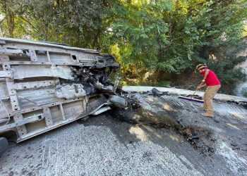 Large Overturned Heavy Vehicle Crushed on Its Side, Debris Scattered on the Road, Worker in Red Shirt and Helmet Sweeping Nearby - Adelante Mty