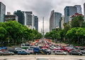 Busy City Boulevard Lined with Green Trees and Tall Office Buildings, Heavy Traffic in Both Directions on a Cloudy Day. - Adelante Mty
