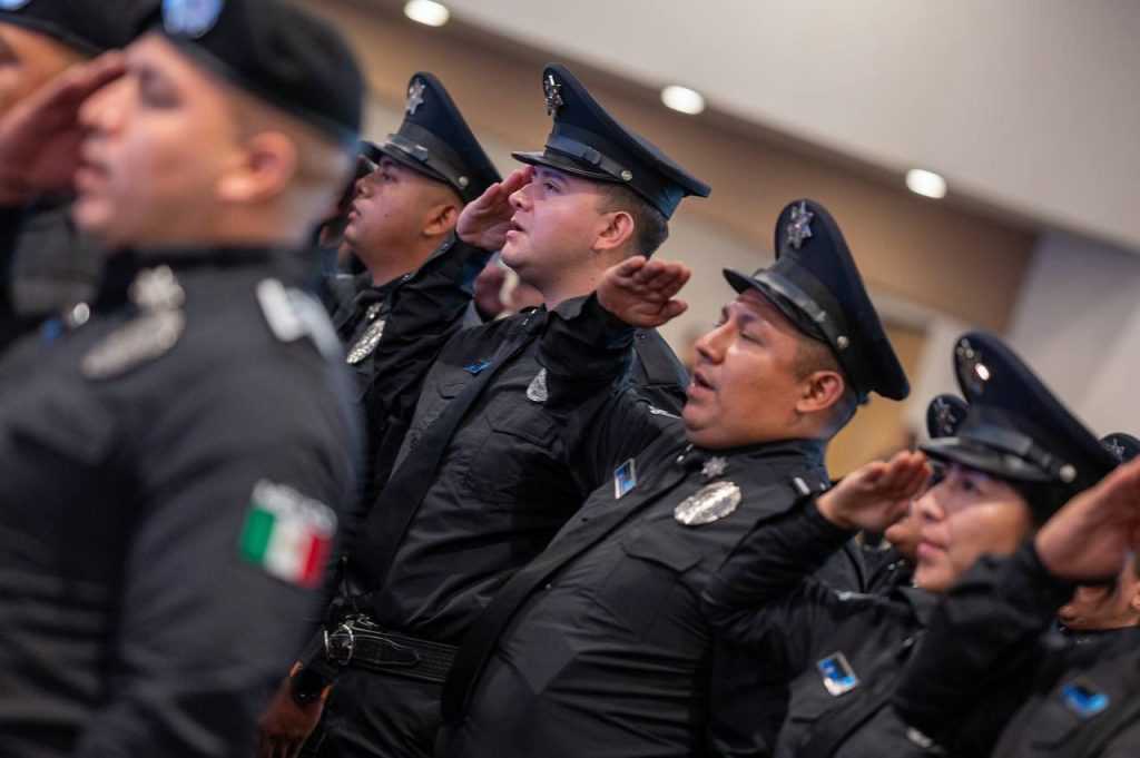 Line of Police Officers in Black Uniforms Saluting in Formation at a Ceremony on an Indoor Setting. - Adelante Mty