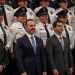 Two Men in Suits Stand in Front of a Line of Uniformed Police Officers at a Formal Event.", - Adelante Mty