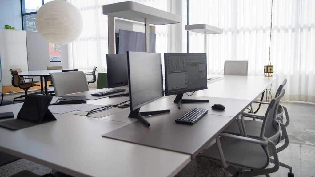 Open-plan Office with White Desks, Multiple Computer Monitors, Keyboards, and Ergonomic Chairs Near Large Windows with Sheer Curtains. - Adelante Mty