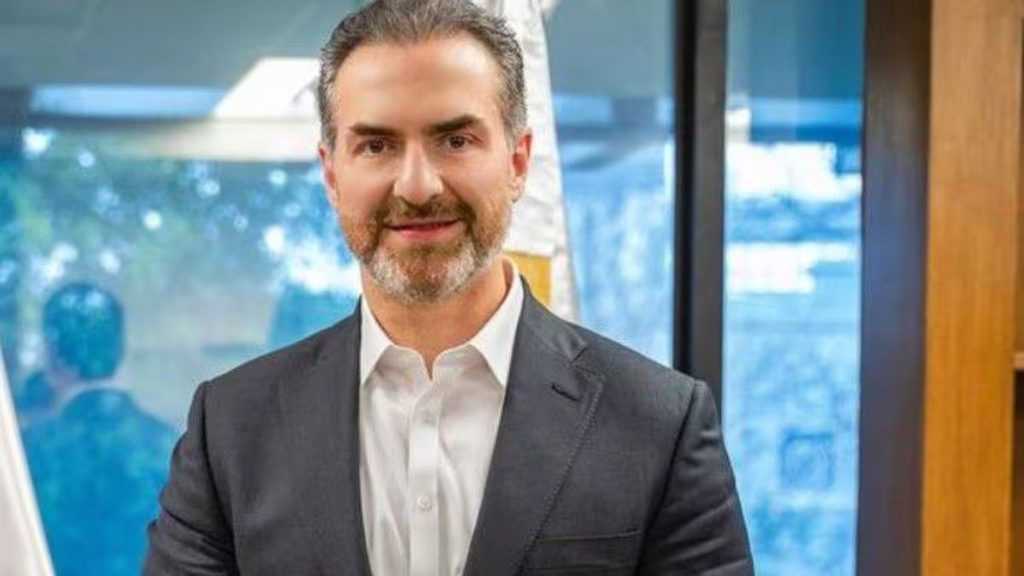 Smiling Man in a Dark Suit and White Shirt Poses in a Modern Office with Glass and Wood Elements. Auto - Adelante Mty