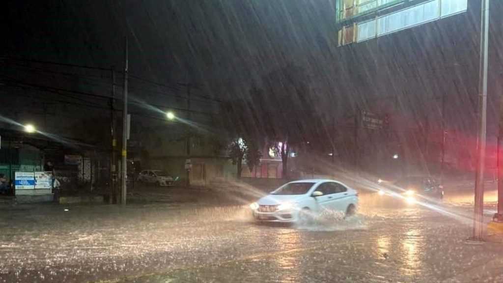 Night Scene of a Car Driving Through a Flooded Street at Night As Heavy Rain Creates Splashes and Reflections from Headlights and Streetlights. - Adelante Mty
