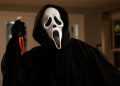 Person in a Black Hooded Cloak Wearing a Ghostface Mask Raises a Blood-stained Knife in a Dimly Lit Room. - Adelante Mty