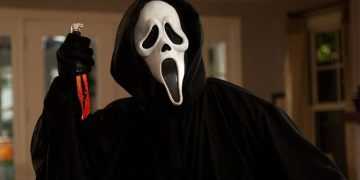 Person in a Black Hooded Cloak Wearing a Ghostface Mask Raises a Blood-stained Knife in a Dimly Lit Room. - Adelante Mty